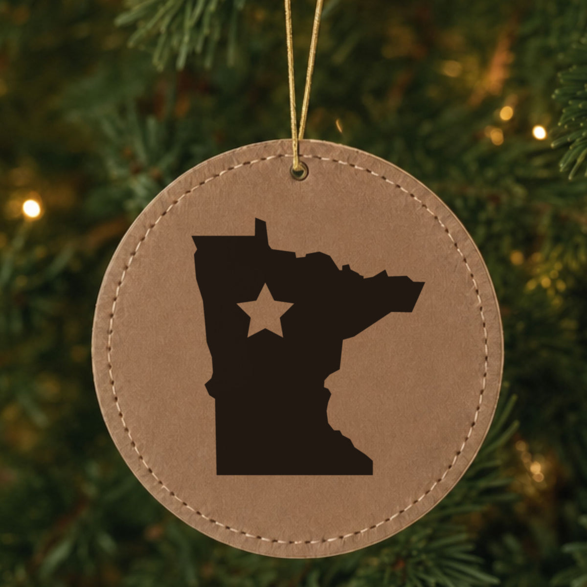 Brown leatherette round Christmas ornament laser engraved with the Minnesota Star Accent design, hanging on a tree