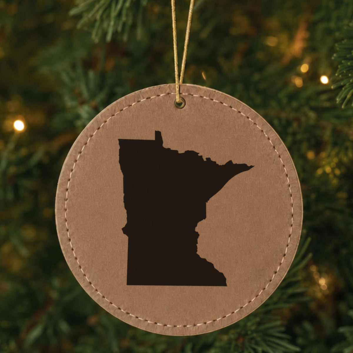 Brown leatherette round Christmas ornament laser engraved with the Minnesota Engraved State design, hanging on a tree