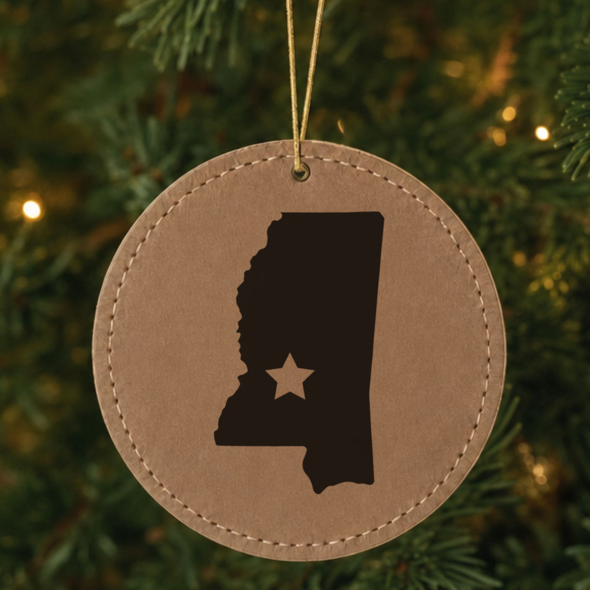 Brown leatherette round Christmas ornament laser engraved with the Mississippi Star Accent design, hanging on a tree