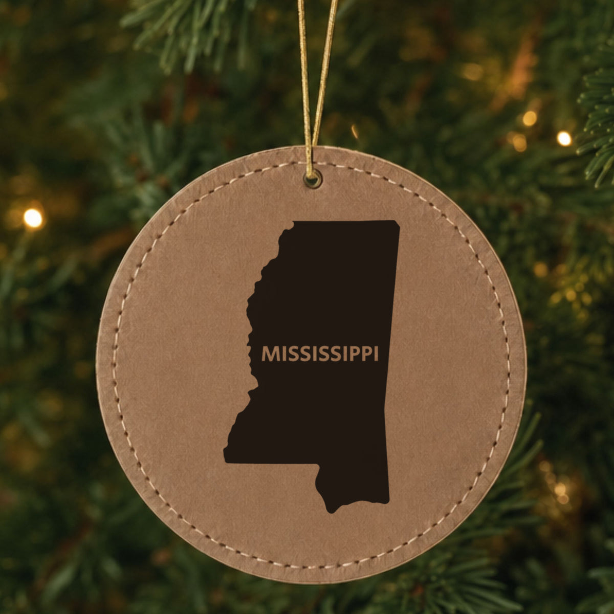 Brown leatherette round Christmas ornament laser engraved with the Mississippi Bold State Name design, hanging on a tree