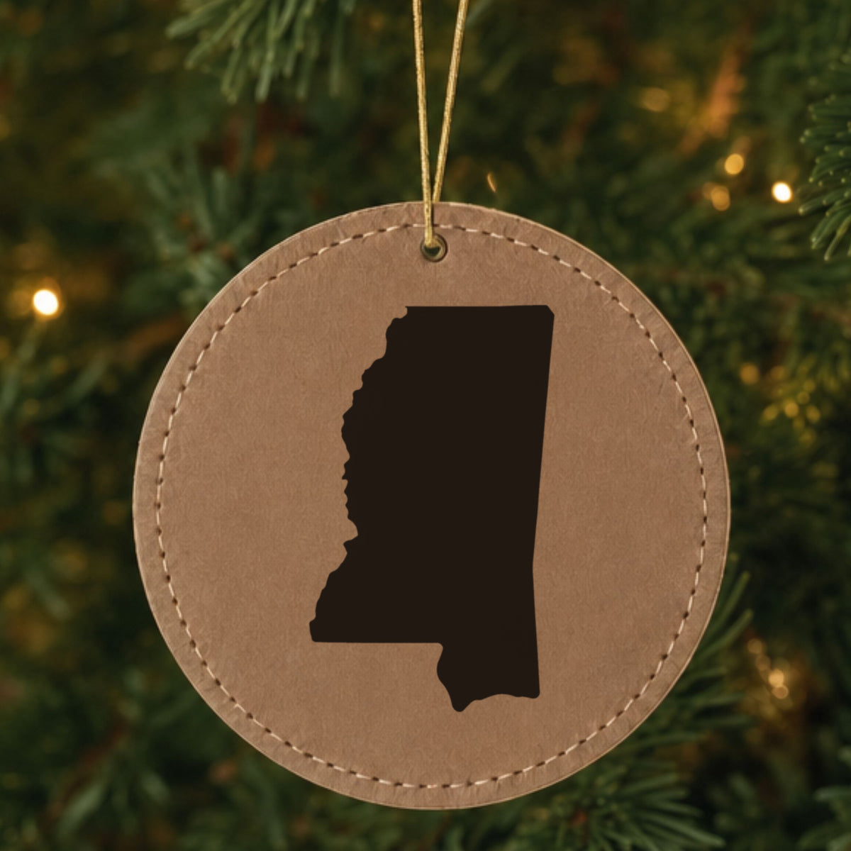 Brown leatherette round Christmas ornament laser engraved with the Mississippi Engraved State design, hanging on a tree