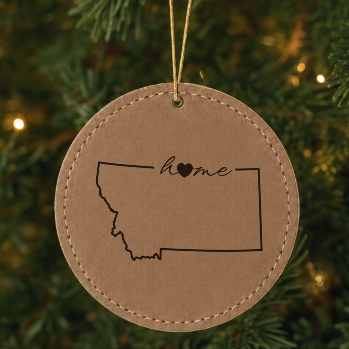 Brown leatherette round Christmas ornament laser engraved with the Montana Home Script & Heart design, hanging on a tree