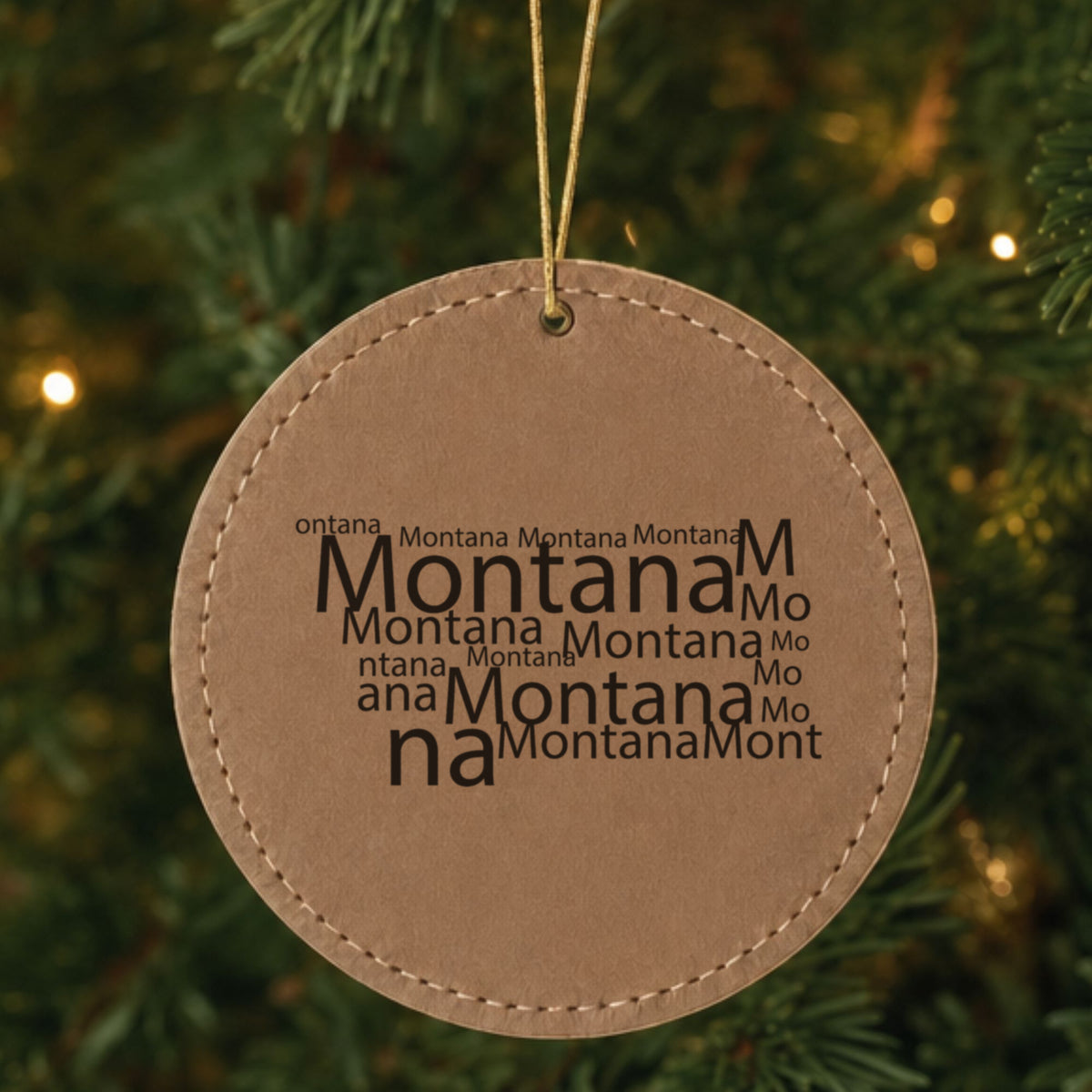 Brown leatherette round Christmas ornament laser engraved with the Montana Word Cloud design, hanging on a tree