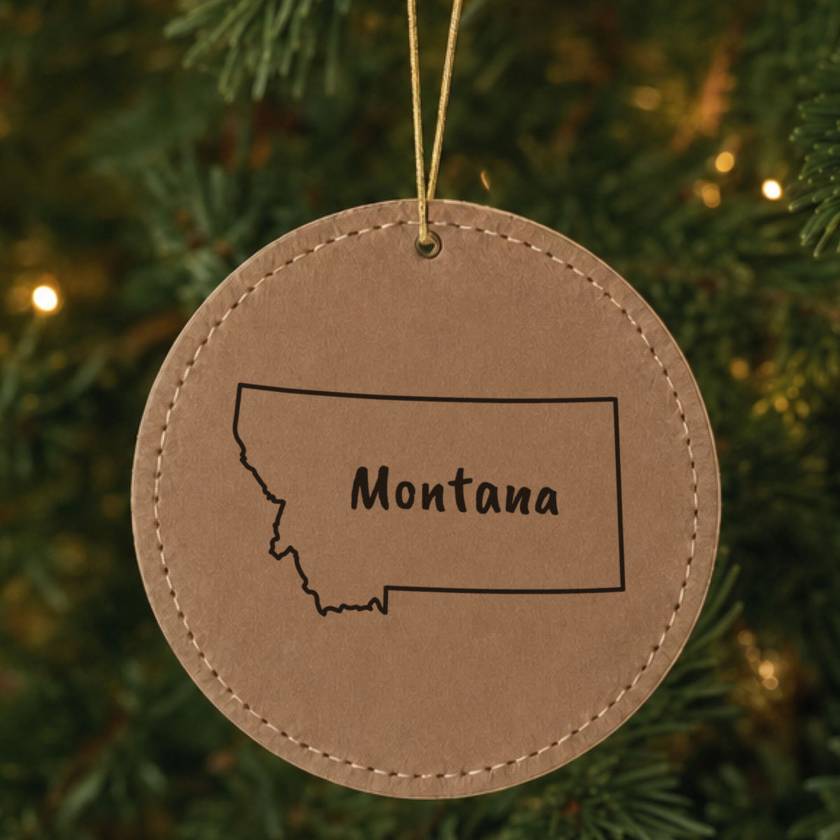 Brown leatherette round Christmas ornament laser engraved with the Montana Brush Lettering design, hanging on a tree