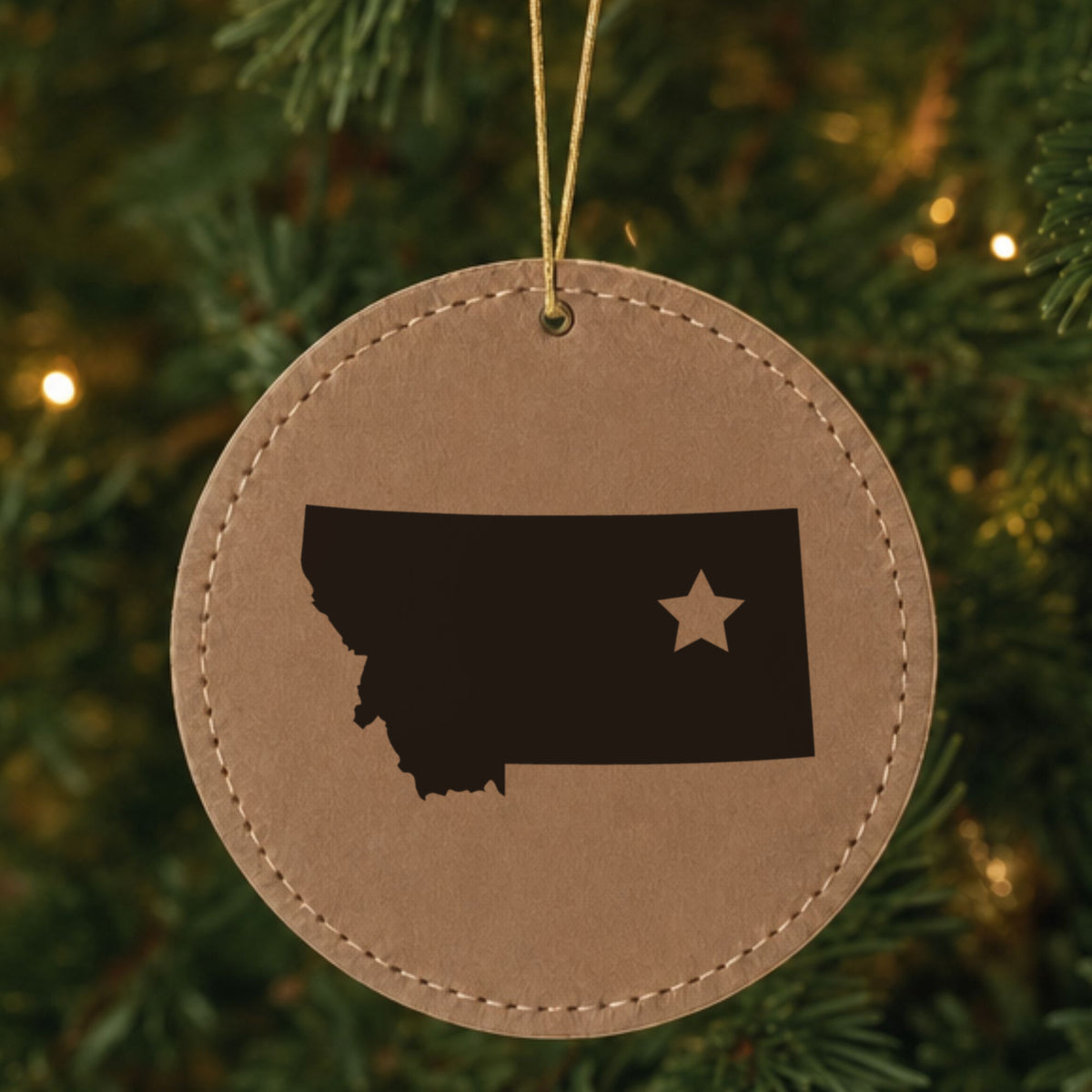 Brown leatherette round Christmas ornament laser engraved with the Montana Star Accent design, hanging on a tree
