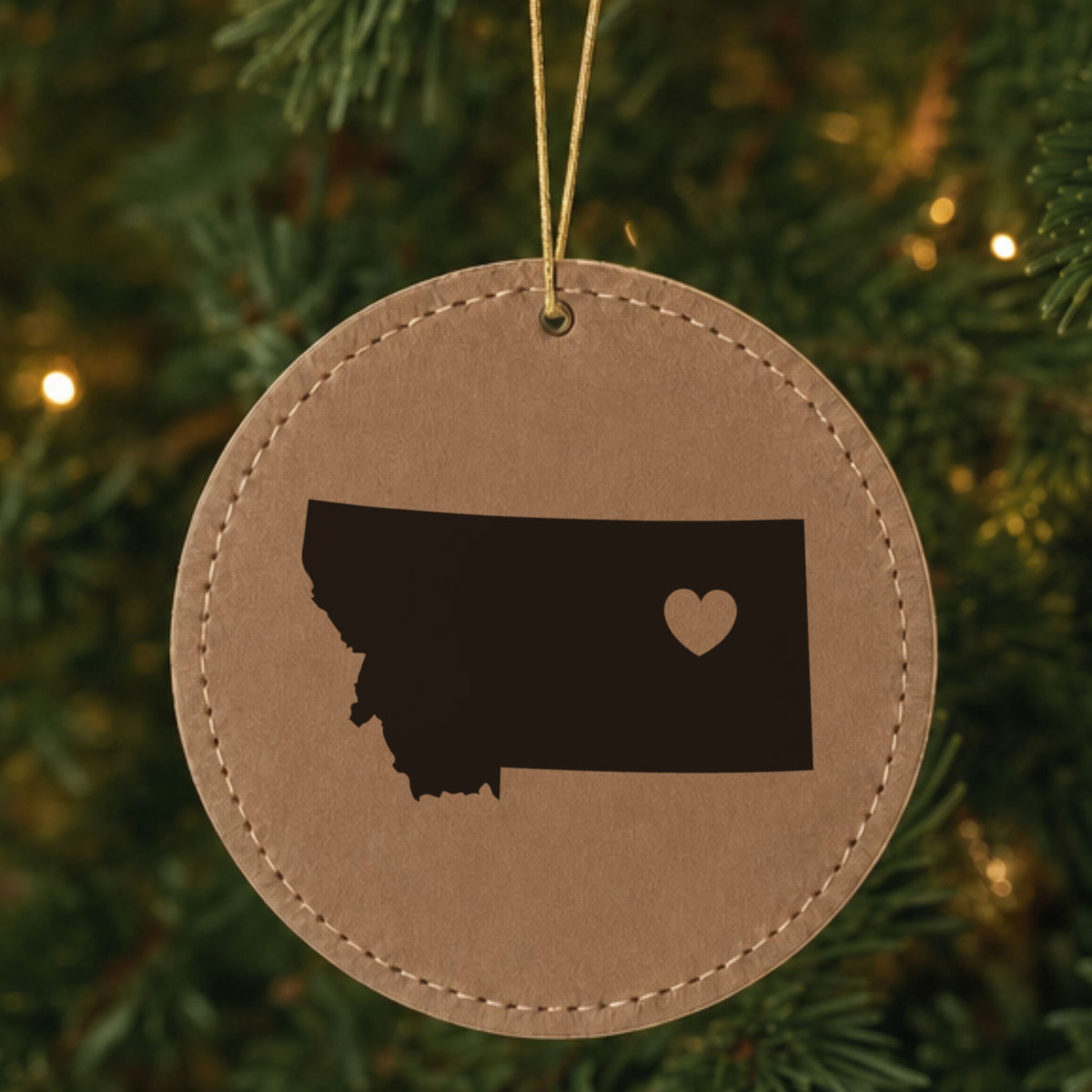 Brown leatherette round Christmas ornament laser engraved with the Montana Heart Accent design, hanging on a tree