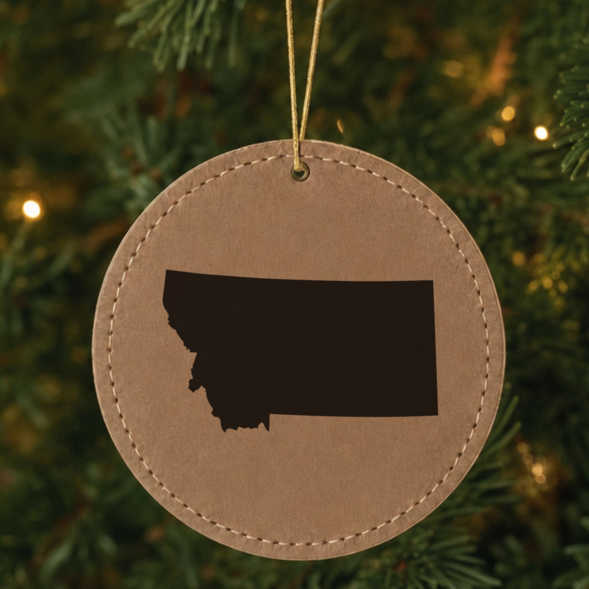 Brown leatherette round Christmas ornament laser engraved with the Montana Engraved State design, hanging on a tree