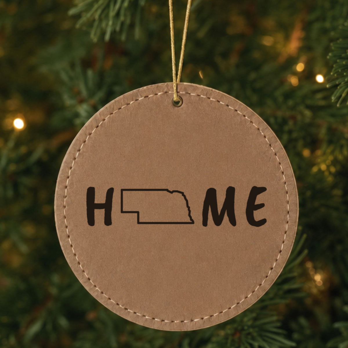 Brown leatherette round Christmas ornament laser engraved with the Nebraska HOME Outline design, hanging on a tree