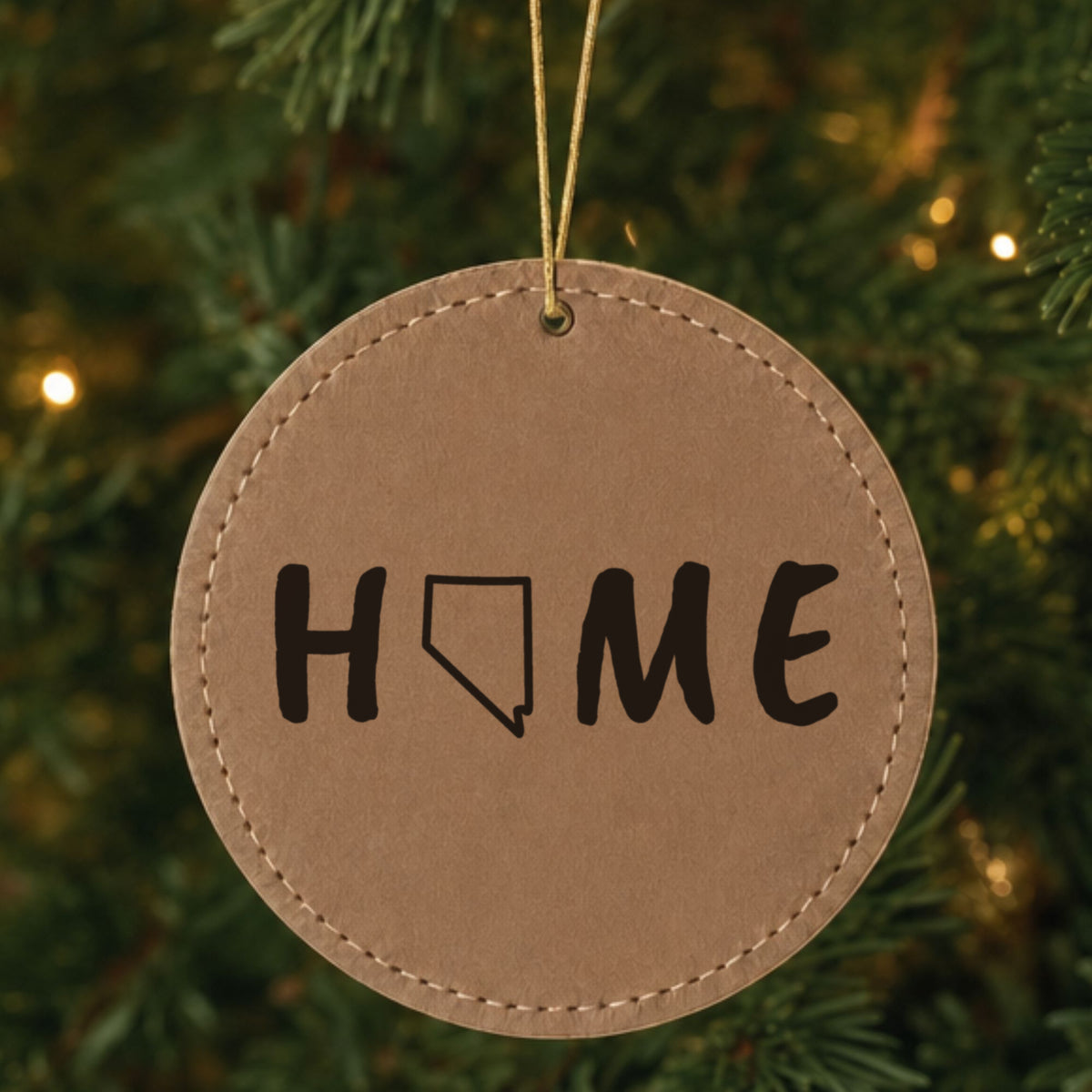 Brown leatherette round Christmas ornament laser engraved with the Nevada HOME Outline design, hanging on a tree