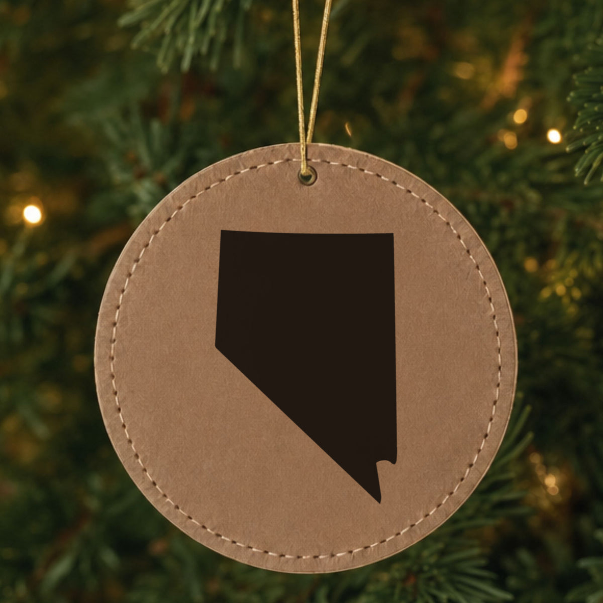 Brown leatherette round Christmas ornament laser engraved with the Nevada Engraved State design, hanging on a tree