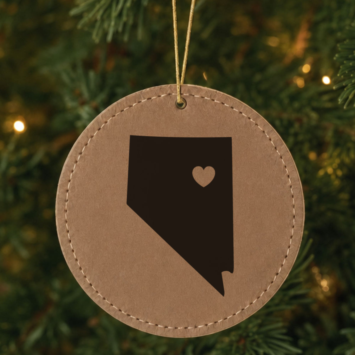 Brown leatherette round Christmas ornament laser engraved with the Nevada Heart Accent design, hanging on a tree
