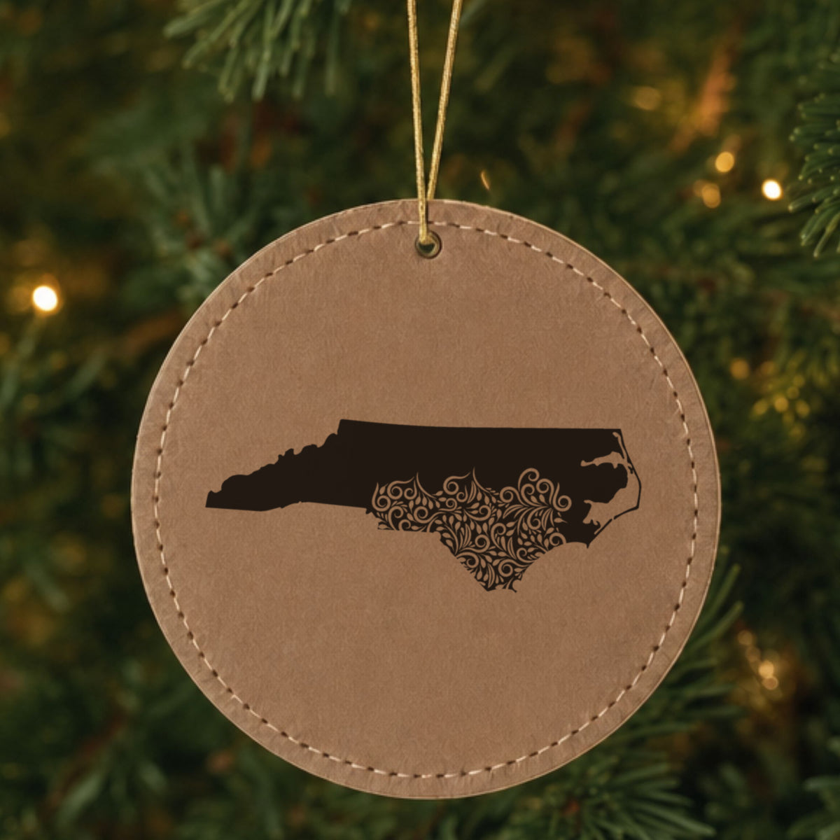 Brown leatherette round Christmas ornament laser engraved with the North Carolina Floral Damask design, hanging on a tree