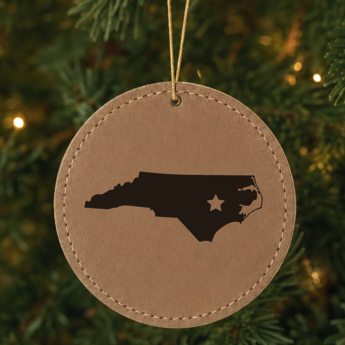 Brown leatherette round Christmas ornament laser engraved with the North Carolina Star Accent design, hanging on a tree
