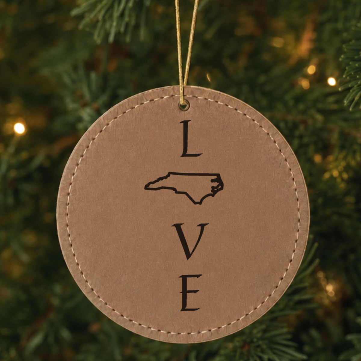 Brown leatherette round Christmas ornament laser engraved with the North Carolina LOVE Stacked design, hanging on a tree
