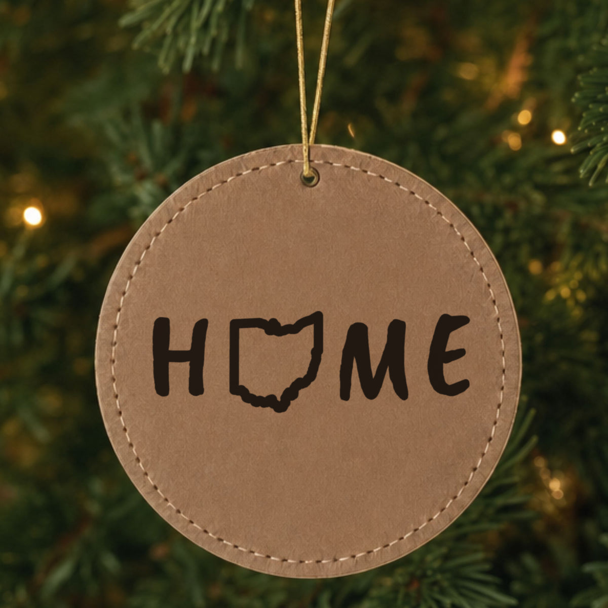 Brown leatherette round Christmas ornament laser engraved with the Ohio HOME Outline design, hanging on a tree
