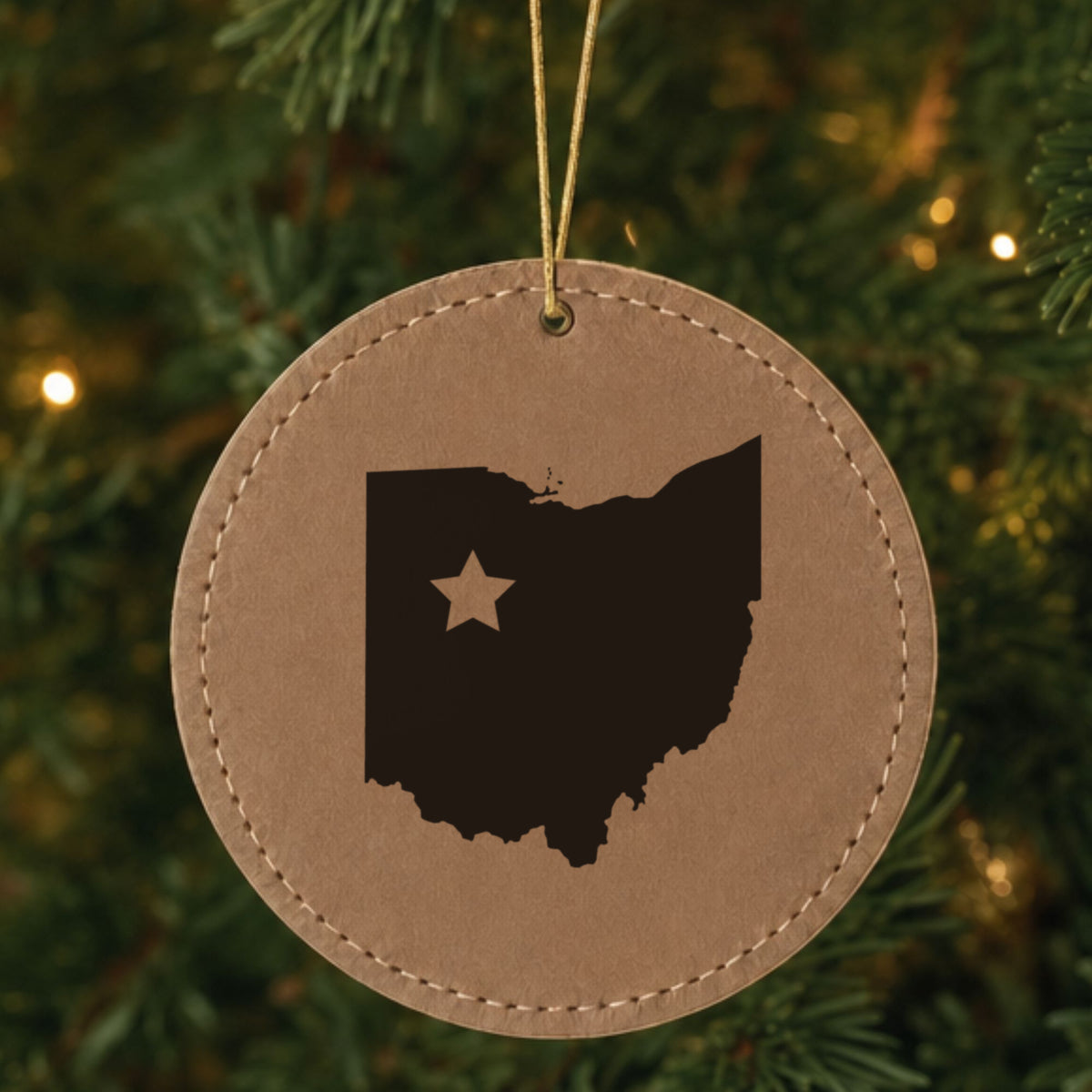 Brown leatherette round Christmas ornament laser engraved with the Ohio Star Accent design, hanging on a tree
