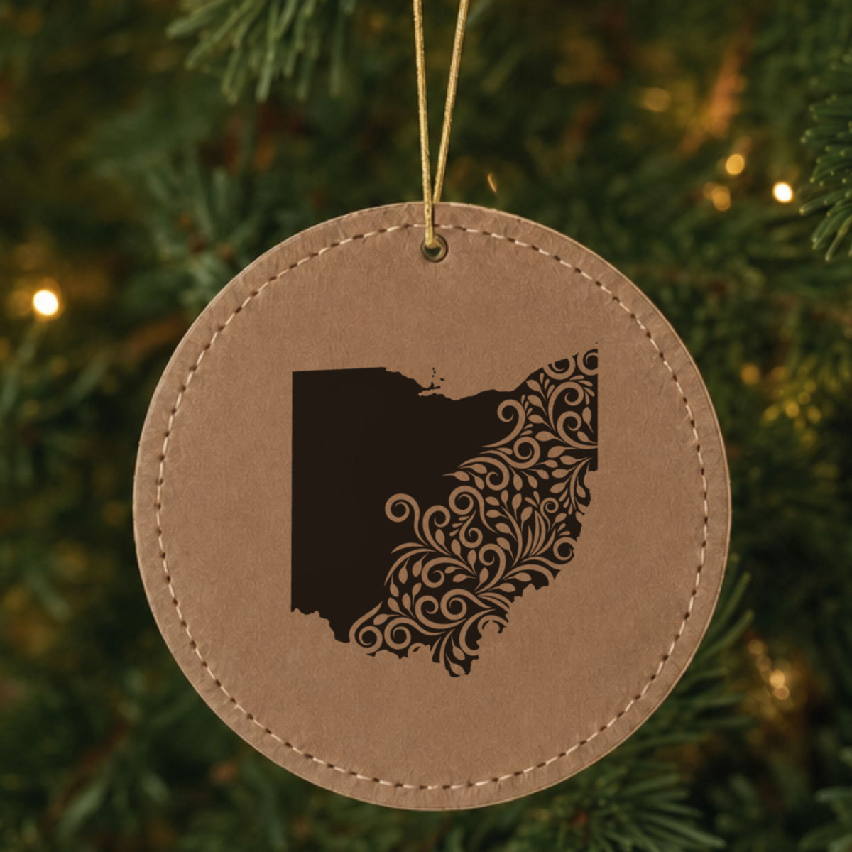 Brown leatherette round Christmas ornament laser engraved with the Ohio Floral Damask design, hanging on a tree