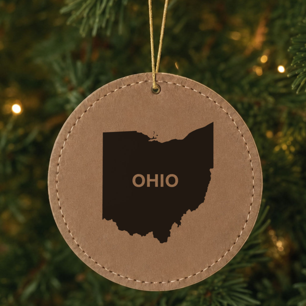Brown leatherette round Christmas ornament laser engraved with the Ohio Bold State Name design, hanging on a tree
