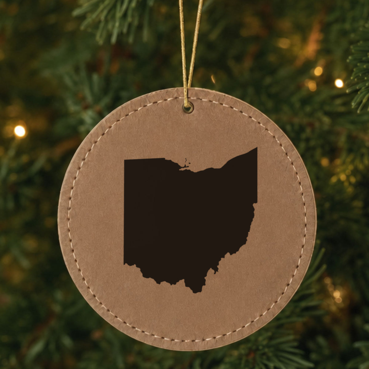 Brown leatherette round Christmas ornament laser engraved with the Ohio Engraved State design, hanging on a tree