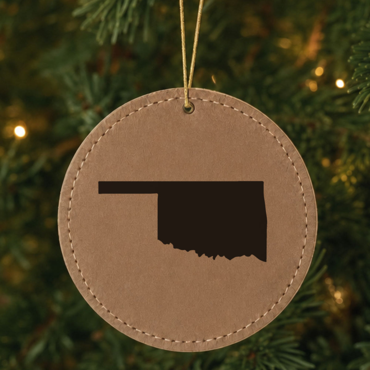 Brown leatherette round Christmas ornament laser engraved with the Oklahoma Engraved State design, hanging on a tree