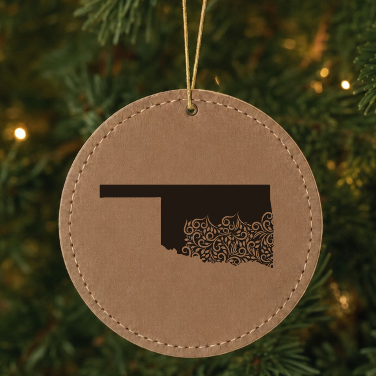 Brown leatherette round Christmas ornament laser engraved with the Oklahoma Floral Damask design, hanging on a tree