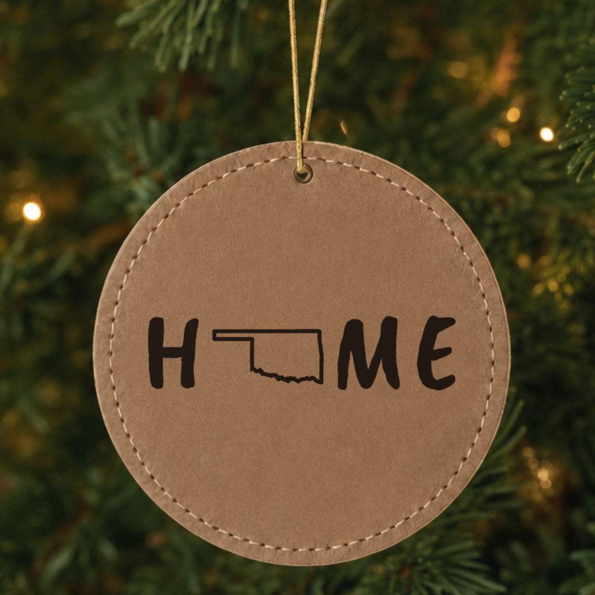 Brown leatherette round Christmas ornament laser engraved with the Oklahoma HOME Outline design, hanging on a tree