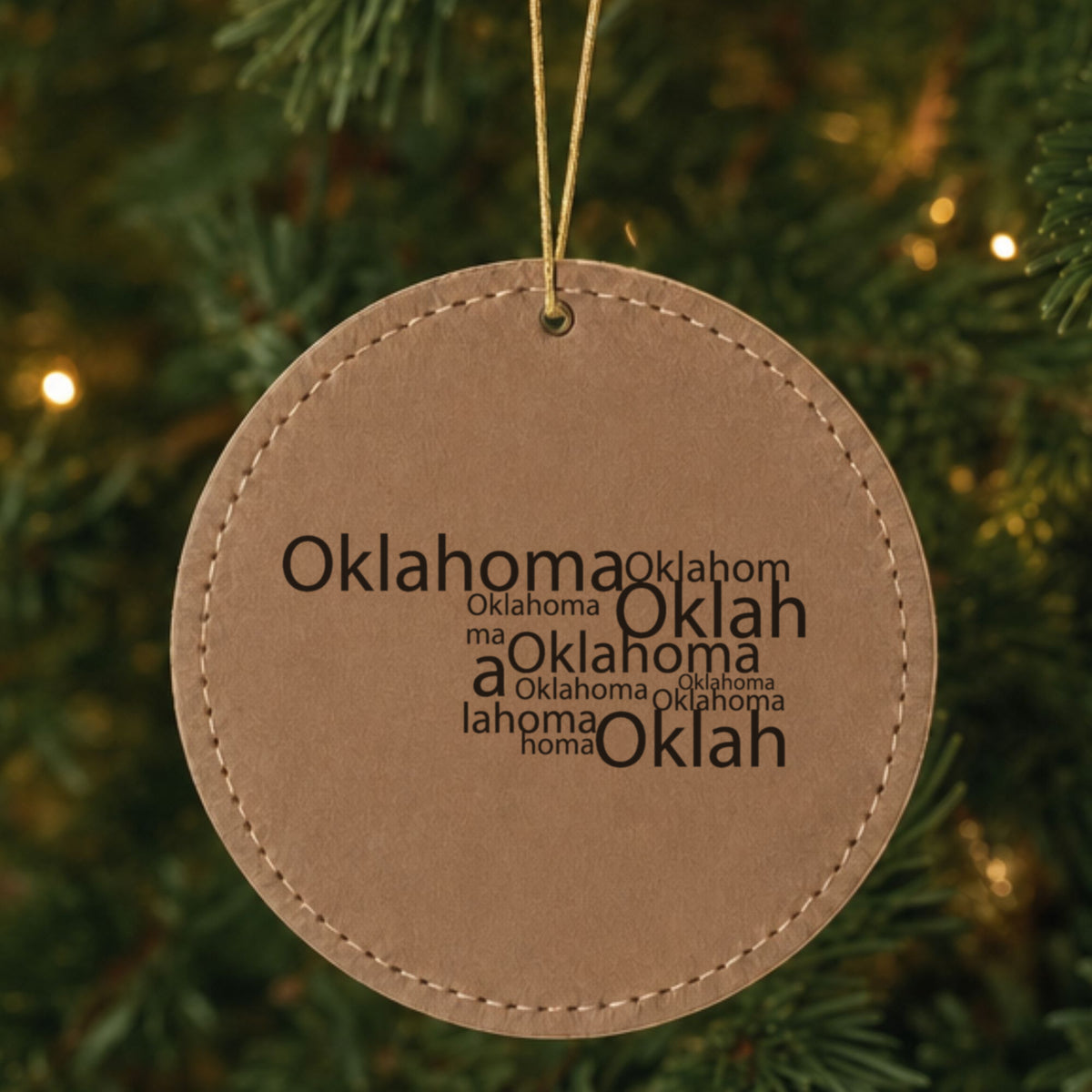 Brown leatherette round Christmas ornament laser engraved with the Oklahoma Word Cloud design, hanging on a tree