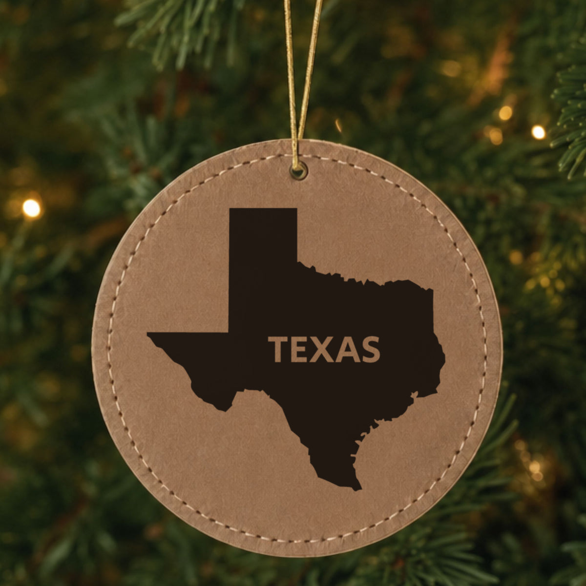 Brown leatherette round Christmas ornament laser engraved with the Texas Bold State Name design, hanging on a tree