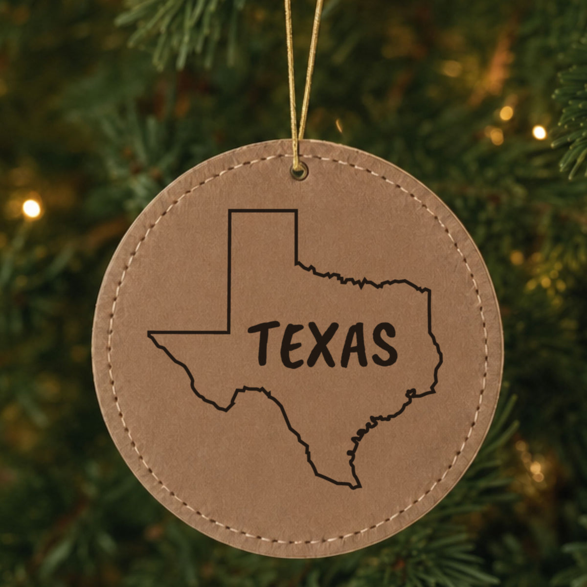Brown leatherette round Christmas ornament laser engraved with the Texas Brush Lettering design, hanging on a tree