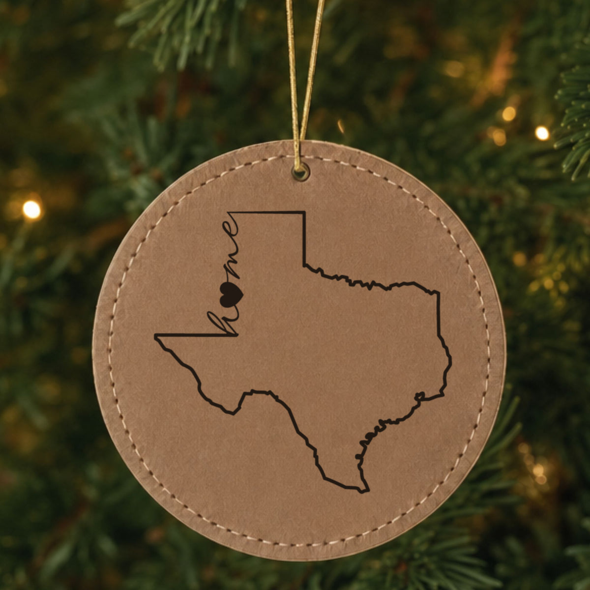 Brown leatherette round Christmas ornament laser engraved with the Texas Home Script & Heart design, hanging on a tree