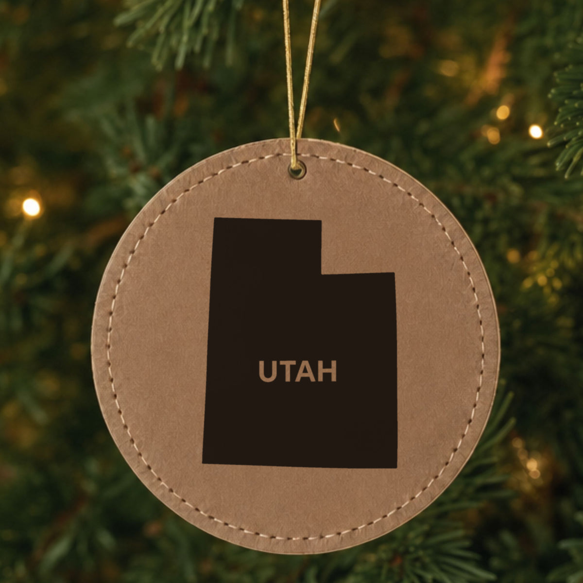 Brown leatherette round Christmas ornament laser engraved with the Utah Bold State Name design, hanging on a tree