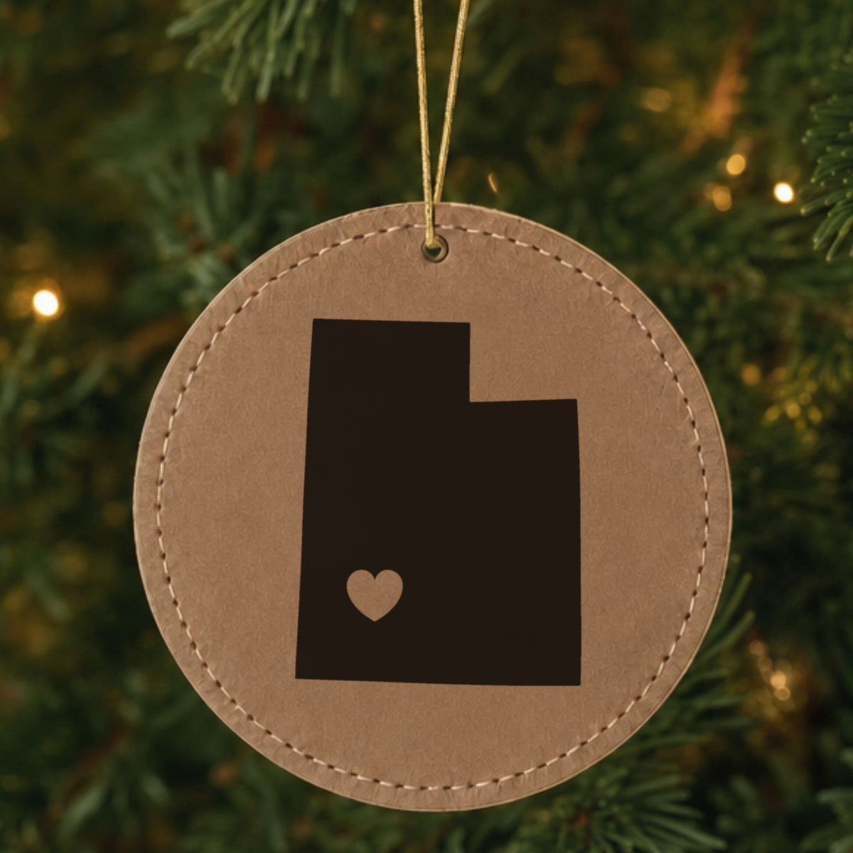 Brown leatherette round Christmas ornament laser engraved with the Utah Heart Accent design, hanging on a tree