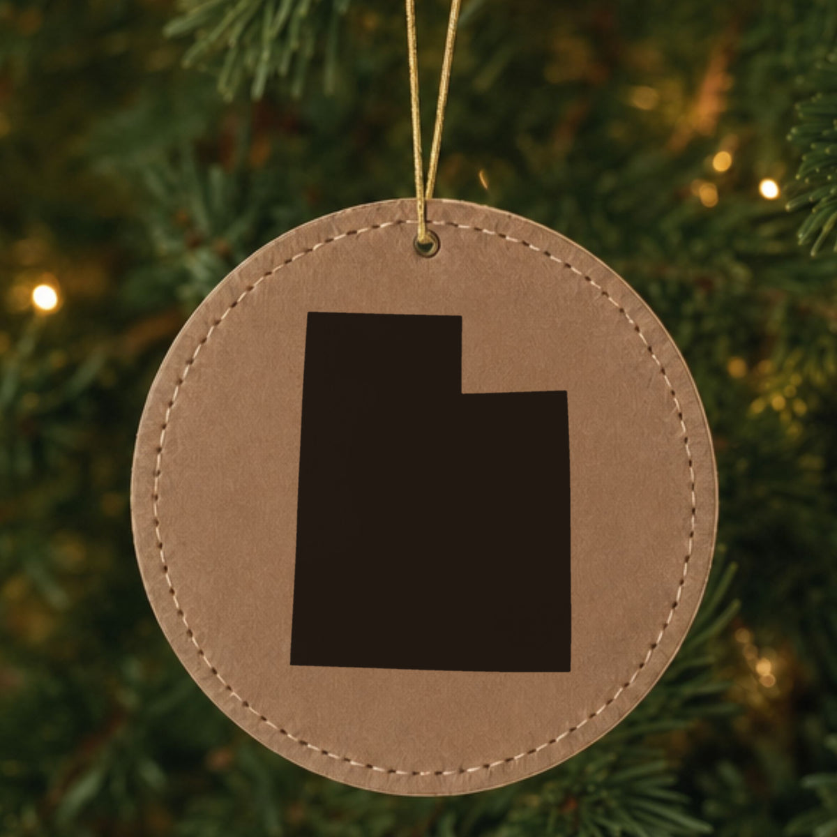 Brown leatherette round Christmas ornament laser engraved with the Utah Engraved State design, hanging on a tree