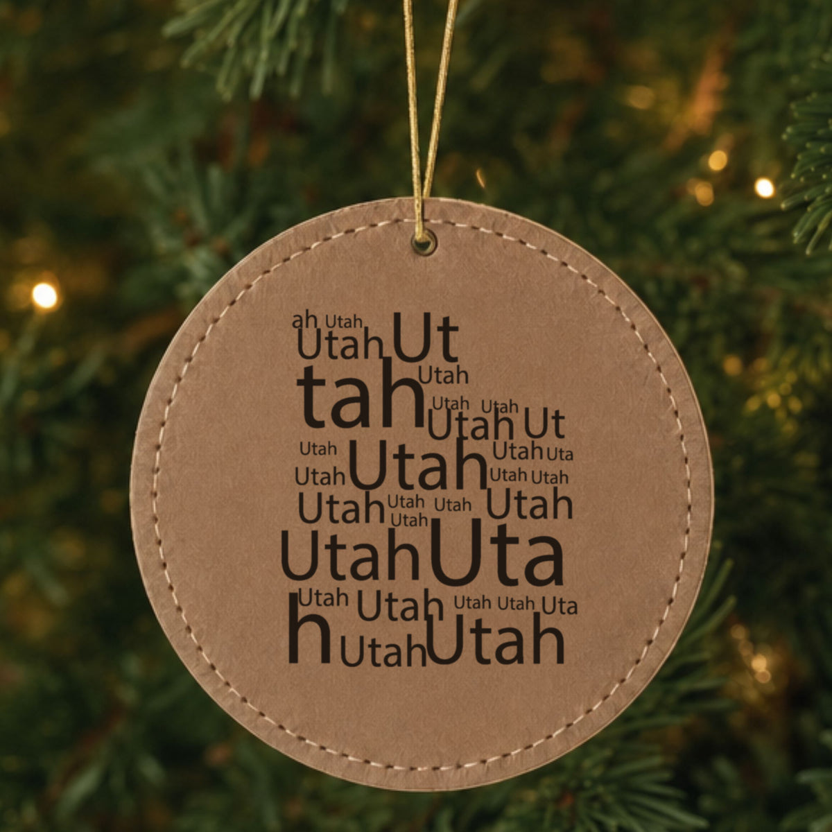 Brown leatherette round Christmas ornament laser engraved with the Utah Word Cloud design, hanging on a tree