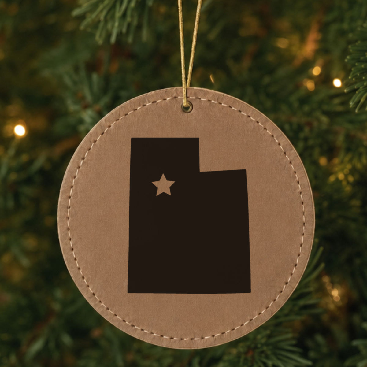 Brown leatherette round Christmas ornament laser engraved with the Utah Star Accent design, hanging on a tree