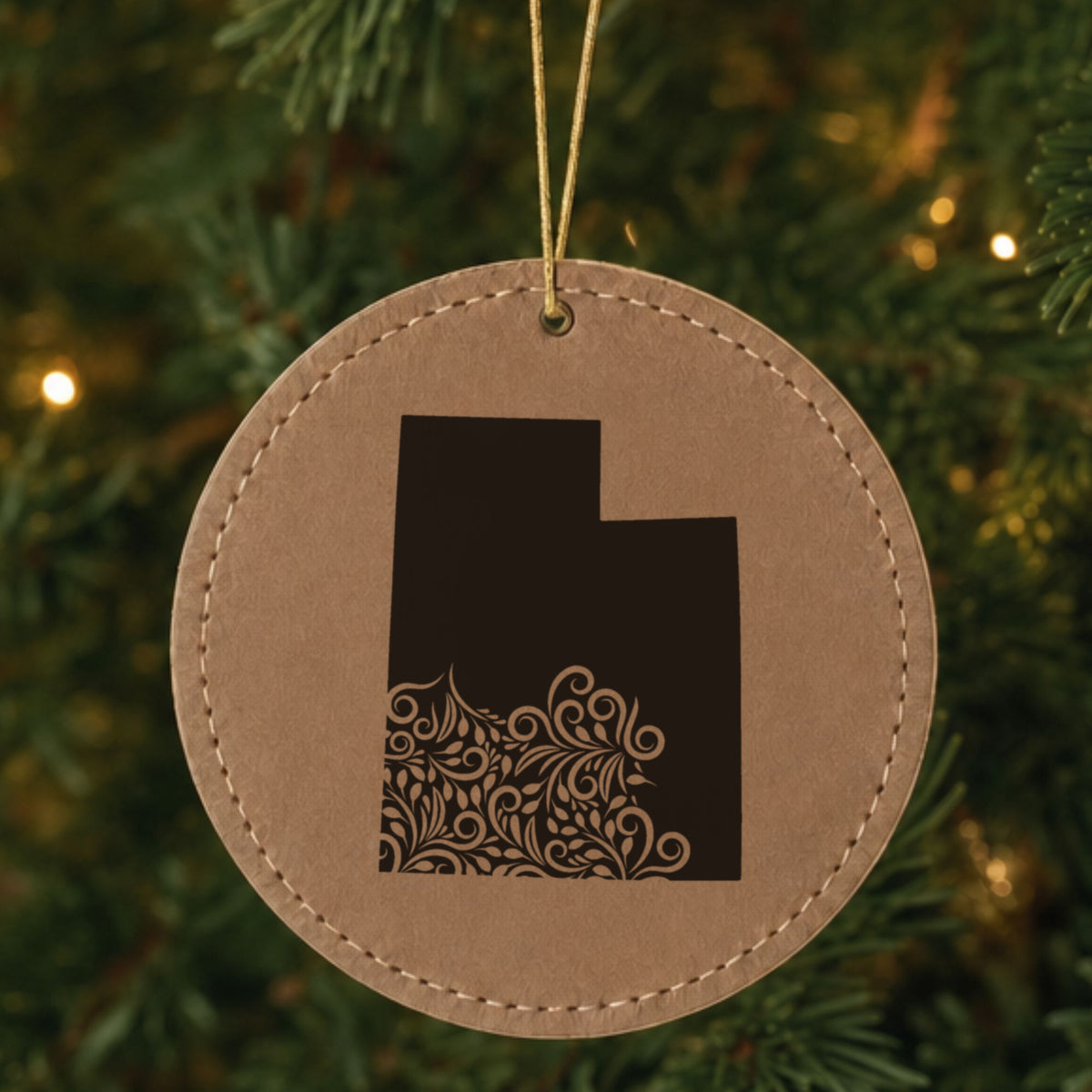 Brown leatherette round Christmas ornament laser engraved with the Utah Floral Damask design, hanging on a tree