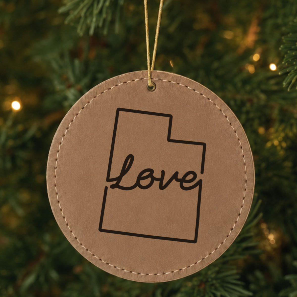 Brown leatherette round Christmas ornament laser engraved with the Utah Hand-Drawn Love design, hanging on a tree