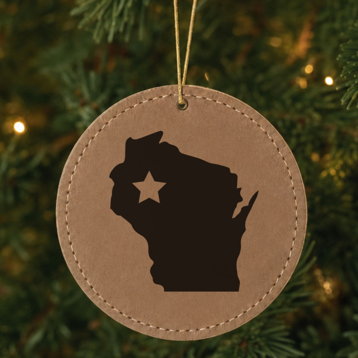 Brown leatherette round Christmas ornament laser engraved with the Wisconsin Star Accent design, hanging on a tree