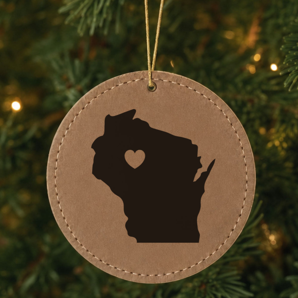 Brown leatherette round Christmas ornament laser engraved with the Wisconsin Heart Accent design, hanging on a tree