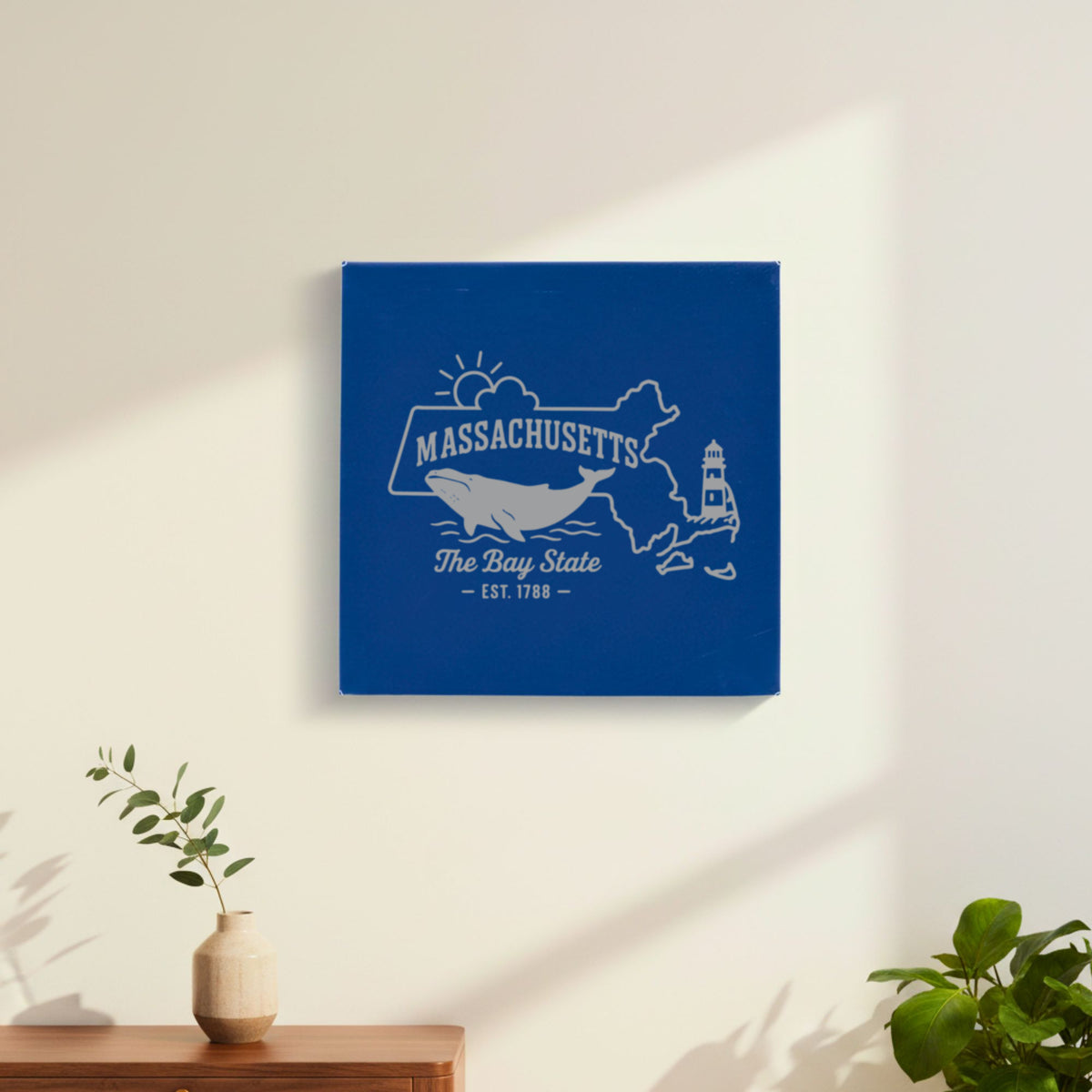 Blue leatherette wall sign engraved with a Massachusetts design of a whale, a lighthouse and the sun over Cape Cod and the islands, hanging on a wall