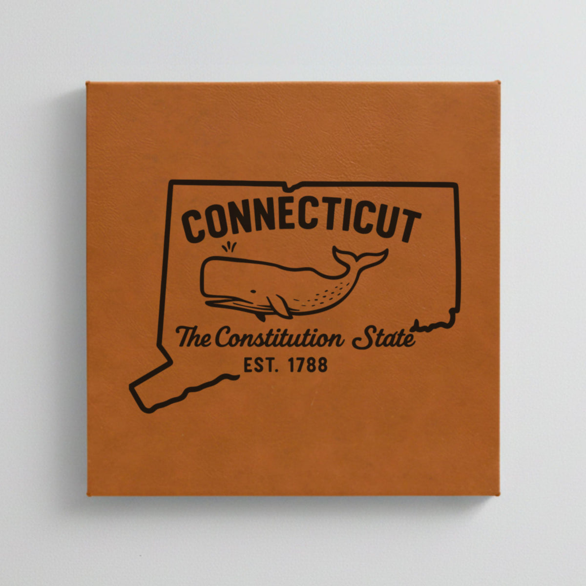 Close up of the Connecticut design engraved on Brown leatherette: a sperm whale, "The Constitution State", EST. 1788