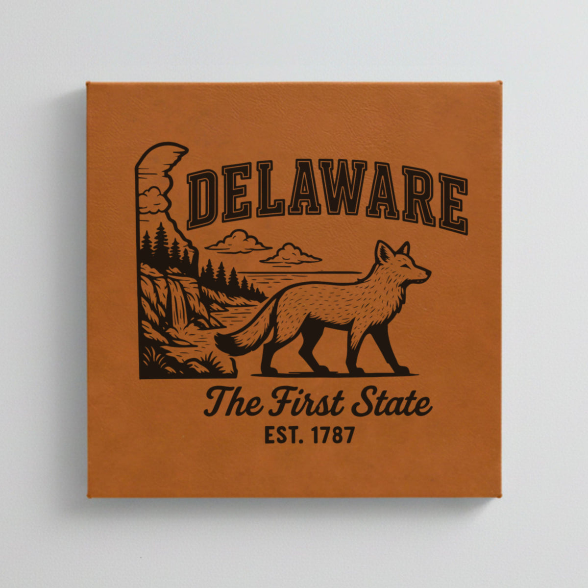 Close up of the Delaware design engraved on Brown leatherette: a gray fox, a waterfall and pine forest, "The First State", EST. 1787