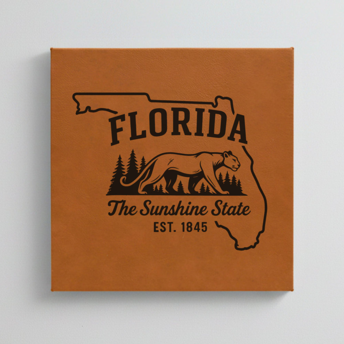 Close up of the Florida design engraved on Brown leatherette: a Florida panther and pine forest, "The Sunshine State", EST. 1845