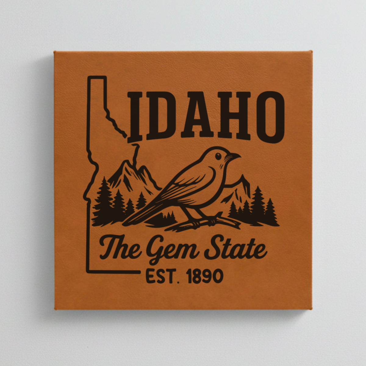 Close up of the Idaho design engraved on Brown leatherette: a mountain bluebird, mountains and pines, "The Gem State", EST. 1890