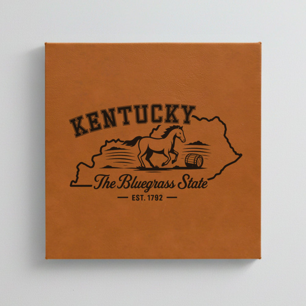 Close up of the Kentucky design engraved on Brown leatherette: a galloping horse and a bourbon barrel, "The Bluegrass State", EST. 1792