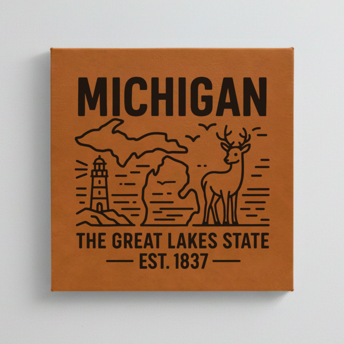 Close up of the Michigan design engraved on Brown leatherette: a lighthouse, a whitetail buck and both peninsulas, "The Great Lakes State", EST. 1837