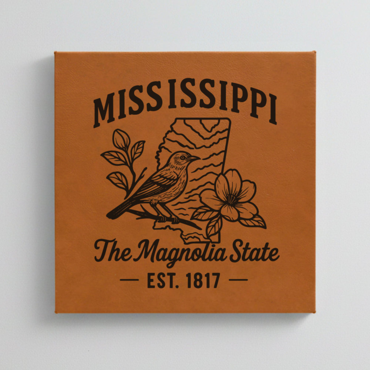 Close up of the Mississippi design engraved on Brown leatherette: a mockingbird and magnolia blossoms, "The Magnolia State", EST. 1817