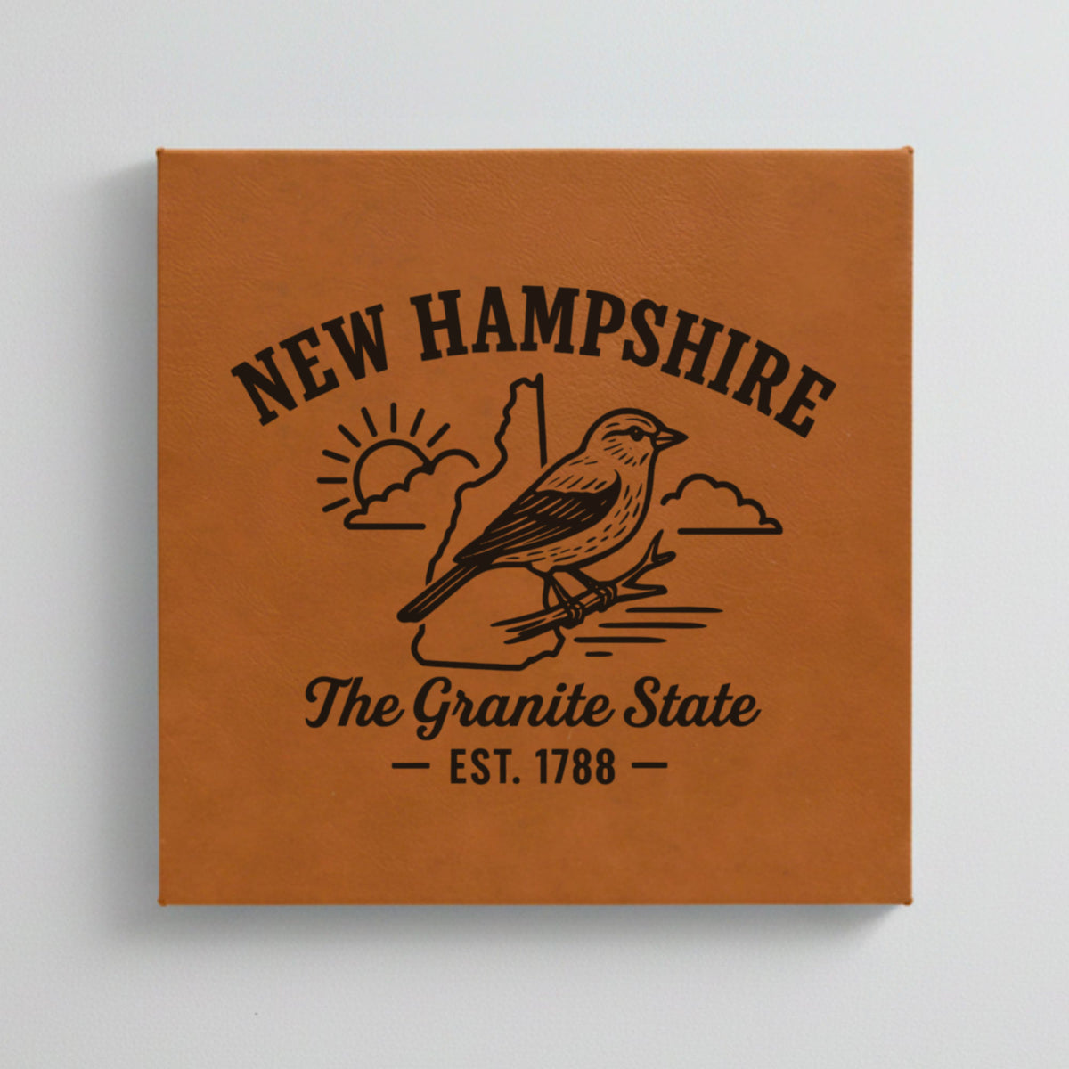 Close up of the New Hampshire design engraved on Brown leatherette: a purple finch, "The Granite State", EST. 1788