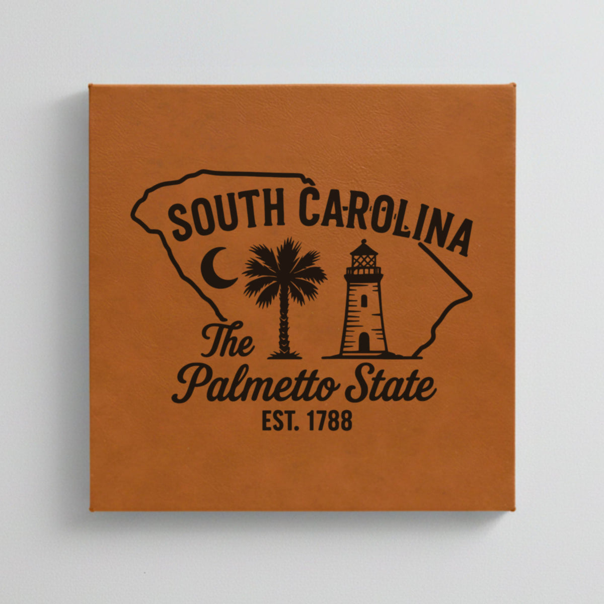 Close up of the South Carolina design engraved on Brown leatherette: a crescent moon, a palmetto tree and a lighthouse, "The Palmetto State", EST. 1788