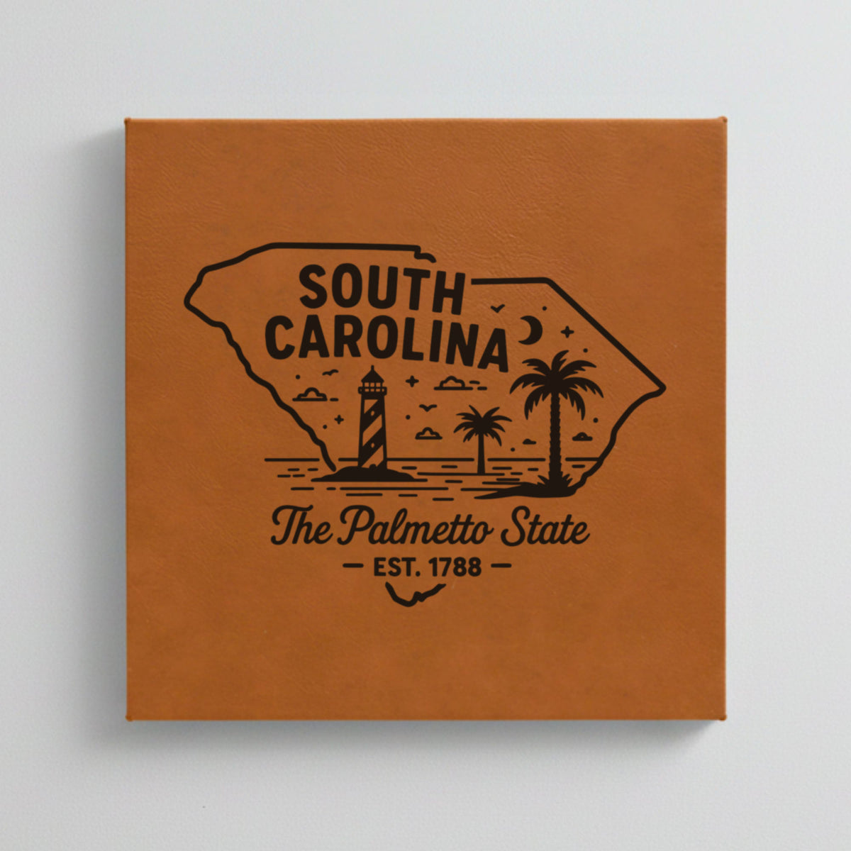 Close up of the South Carolina design engraved on Brown leatherette: a striped lighthouse, palm trees and a beach under a crescent moon, "The Palmetto State", EST. 1788